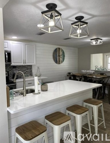 A kitchen with white cabinets and a white countertop with a bar stool in front of it.