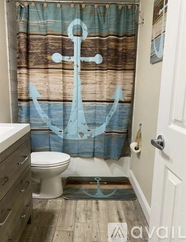 A bathroom with a toilet, sink, and a shower curtain with an anchor design.