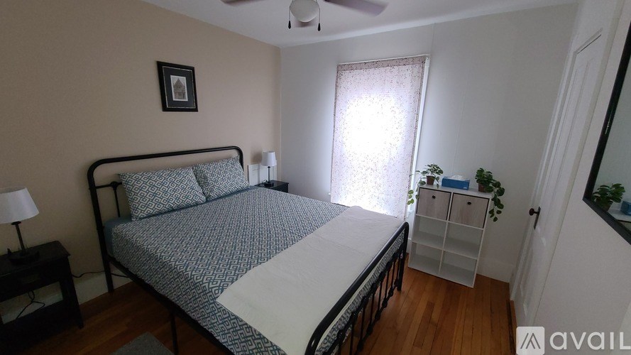 A bedroom with a bed, nightstand, and a plant.