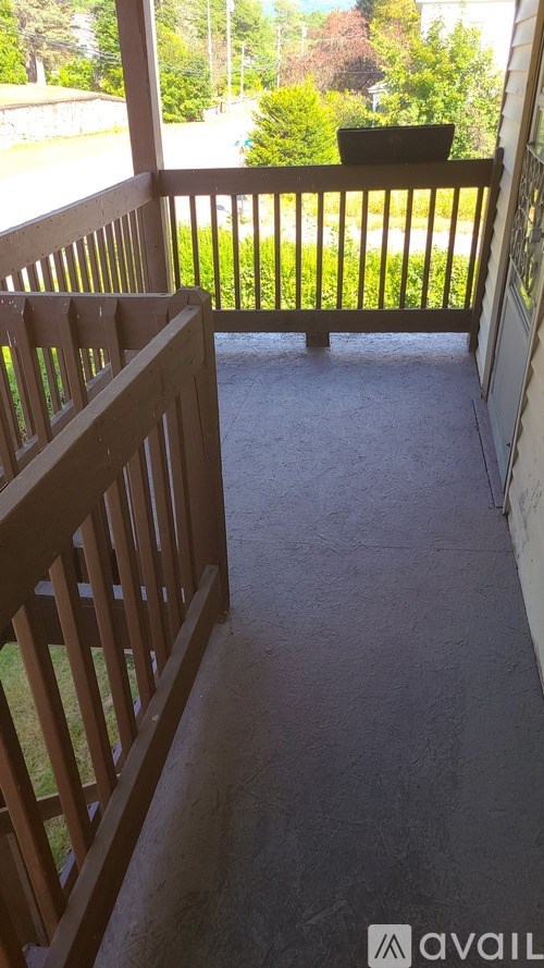 A wooden balcony with a view of a green lawn and trees.
