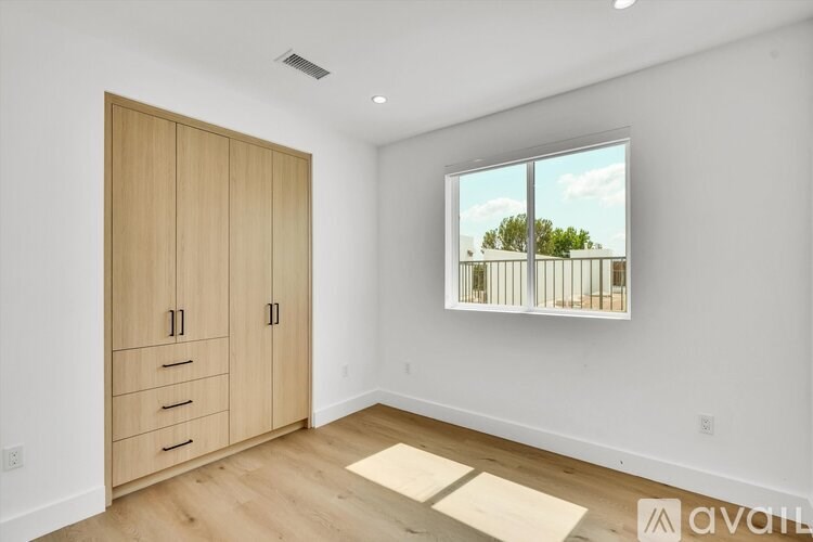 A room with a wooden floor, a large window, and a wooden wardrobe.