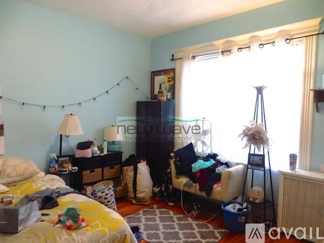 A bedroom with a bed, nightstand, and a window with a view of the street.