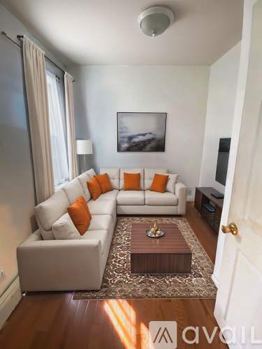 A living room with a white couch and orange pillows.
