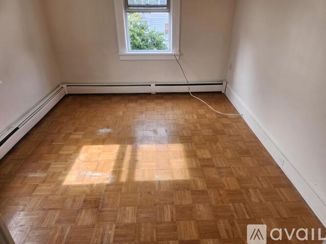 A room with wooden flooring and a window letting in sunlight.
