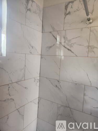 A white marble tiled bathroom wall with a silver grab bar.