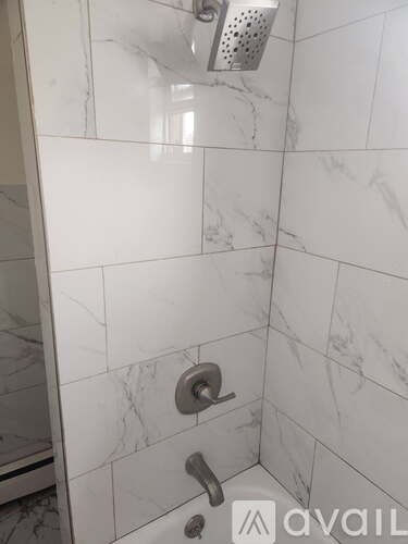 A shower area with a marble tile wall and a silver shower head.