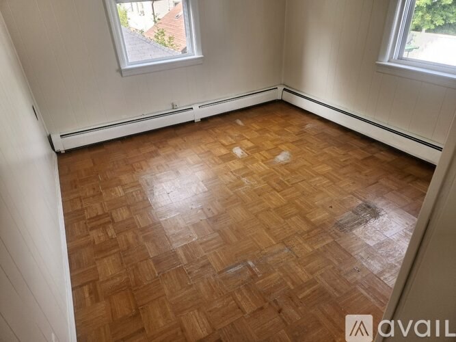 A room with wooden flooring and two windows.