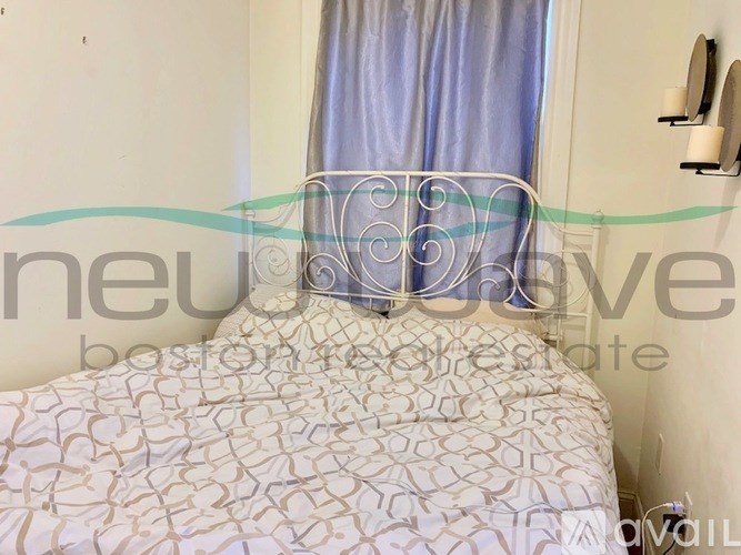 A bed with a white and beige patterned bedspread sits in a room with a blue curtain.