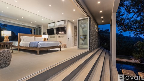 A modern bedroom with a large bed and a balcony overlooking a pool.