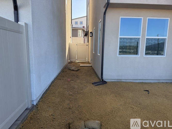 A sandy yard with a white fence and a door leading to another building.