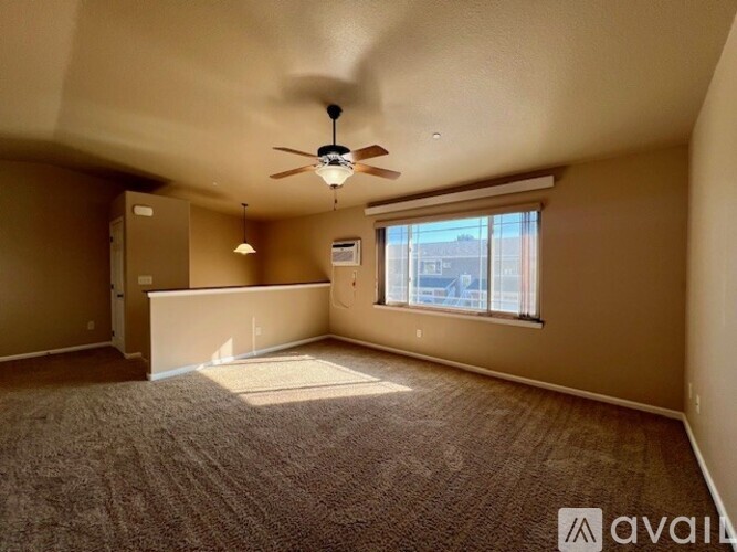 A room with a carpeted floor, a ceiling fan, and a window showing a view of buildings outside.