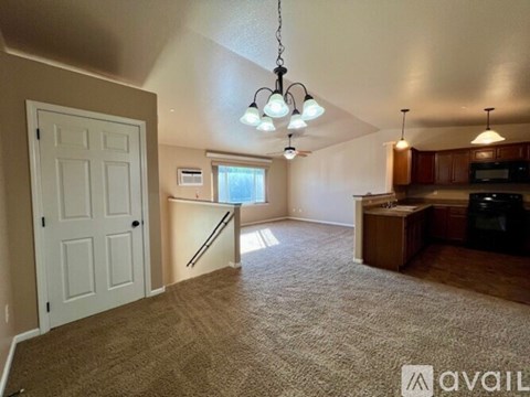 A living room with a carpeted floor and a kitchen area in the background.