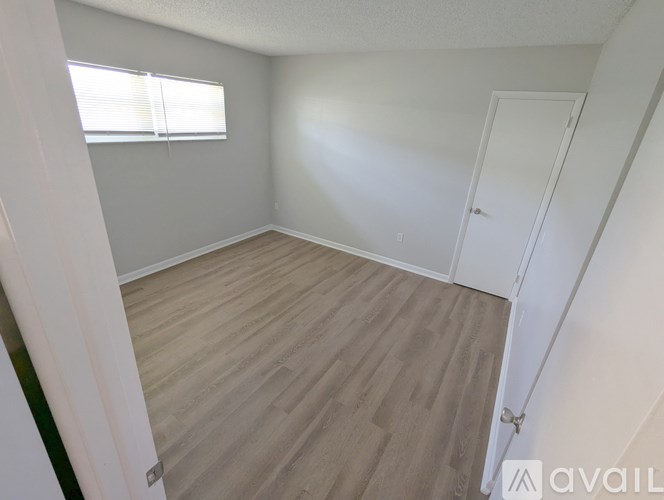 A room with light wood flooring and a window with blinds.