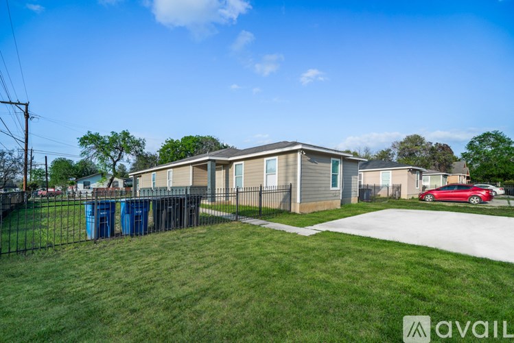 A red car is parked in front of a house with a blue dumpster and a green lawn.