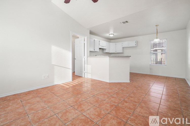 A large empty room with tile flooring and a kitchen area in the background.