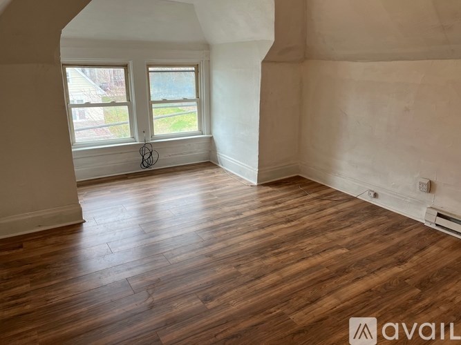 A room with wooden flooring and a window overlooking a green area.