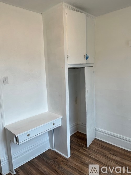 A white desk with drawers is in a room with a white wall and a white door.