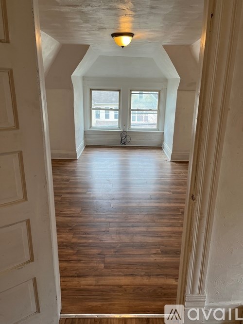 A hallway with wooden floors and white walls leading to a window.