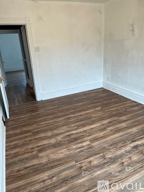 A room with wooden flooring and a doorway leading to another room.