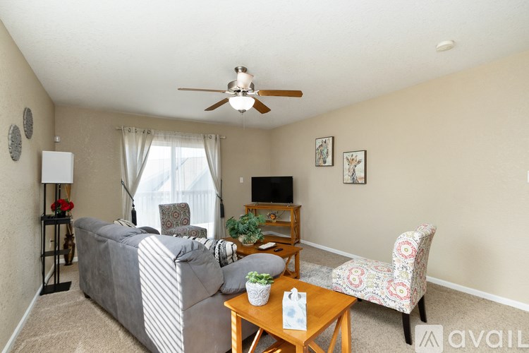 A living room with a grey couch, a wooden coffee table, a television, and a ceiling fan.