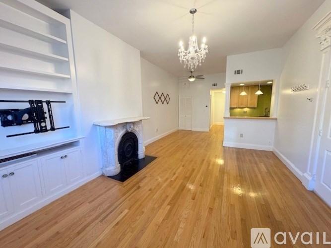 A spacious room with wooden floors and a white fireplace.