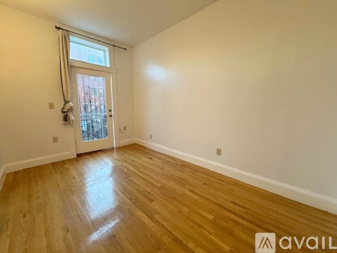 A room with wooden flooring and a window with a view of a building outside.