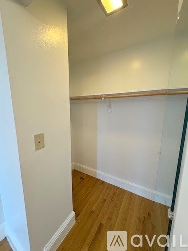 A white wall with a light switch and a wooden floor.
