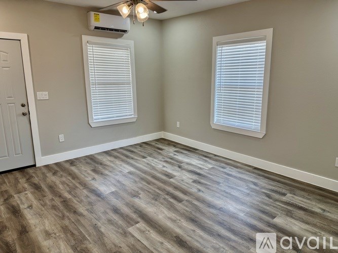 A room with a wooden floor and two windows with blinds.