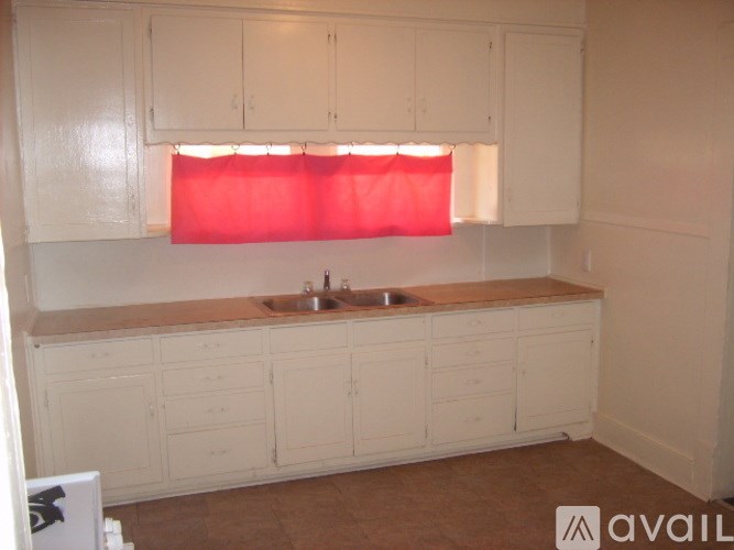 A kitchen with white cabinets and a red curtain.