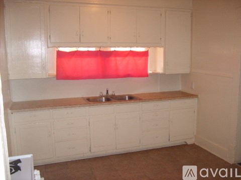 A kitchen with white cabinets and a red curtain.