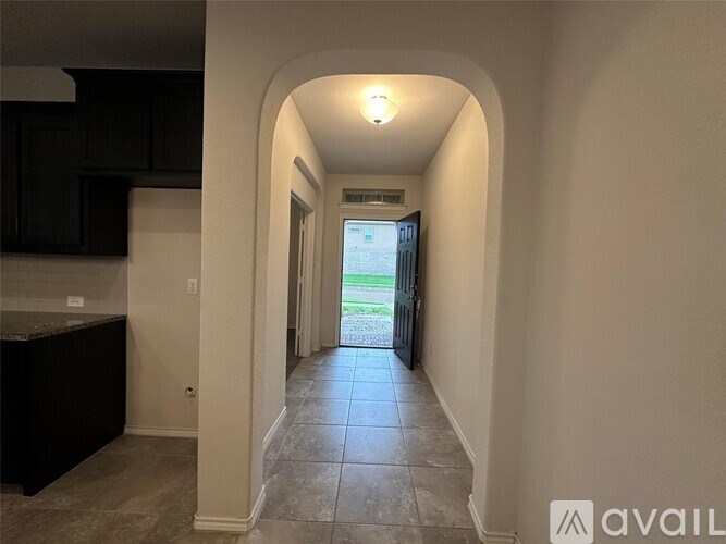 A long hallway with a black counter top and a view of a backyard through a glass door.