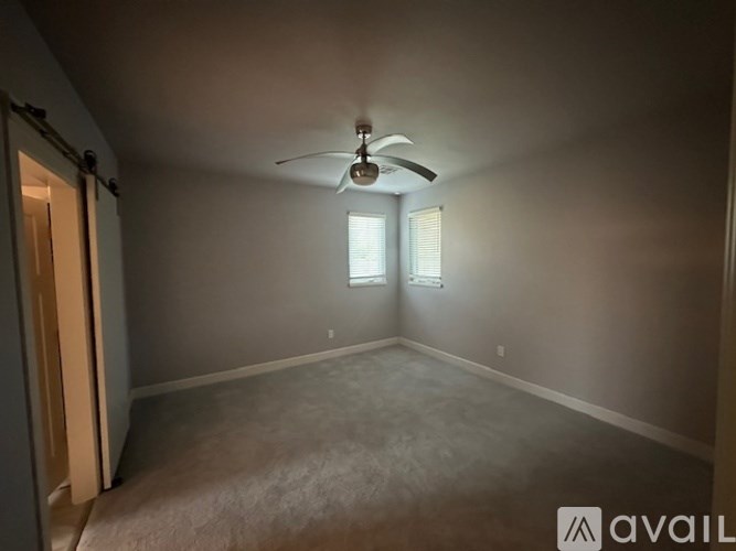 A room with a ceiling fan and two windows.