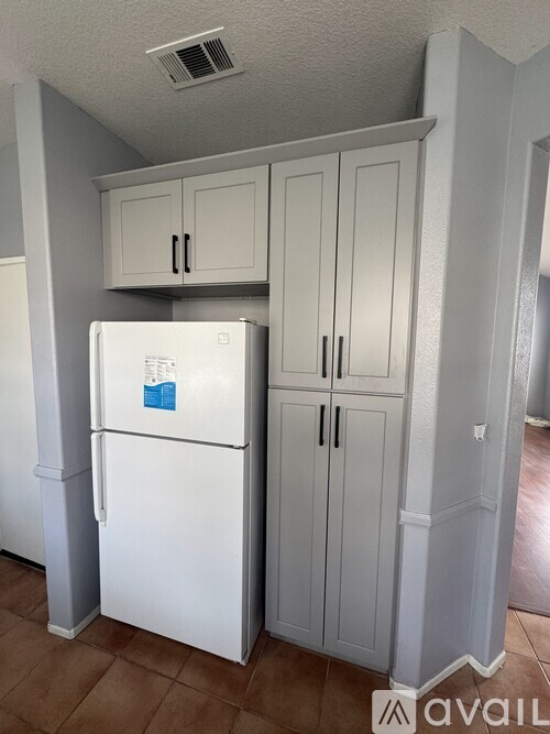 A white fridge in a kitchen with cabinets above it.