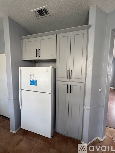 A white fridge in a kitchen with cabinets above it.