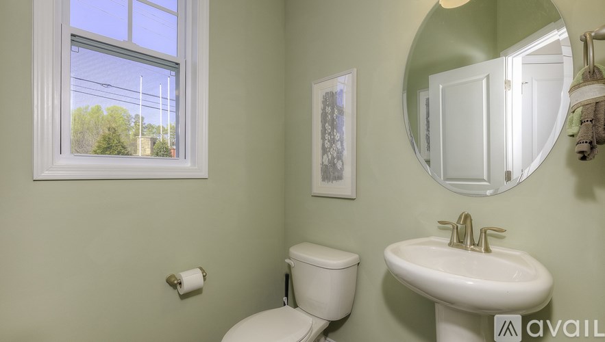 A bathroom with a toilet, sink, mirror, and a window.