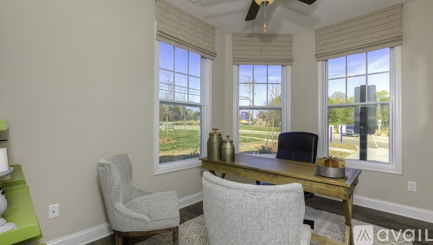 A room with a desk, chairs and a ceiling fan.