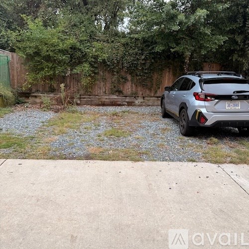 A silver car is parked in a driveway with a gravel area and a wooden fence.
