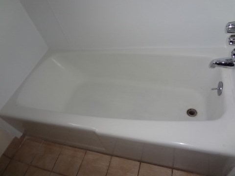 A white bathtub with a faucet and a drain is in a bathroom.