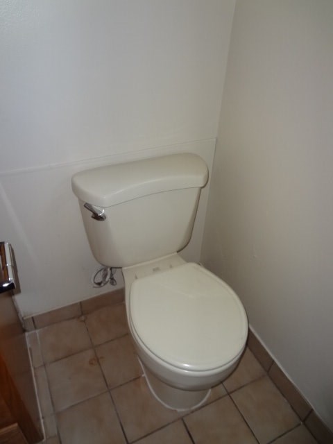 A white toilet with a white tank is in a bathroom with beige tiles.