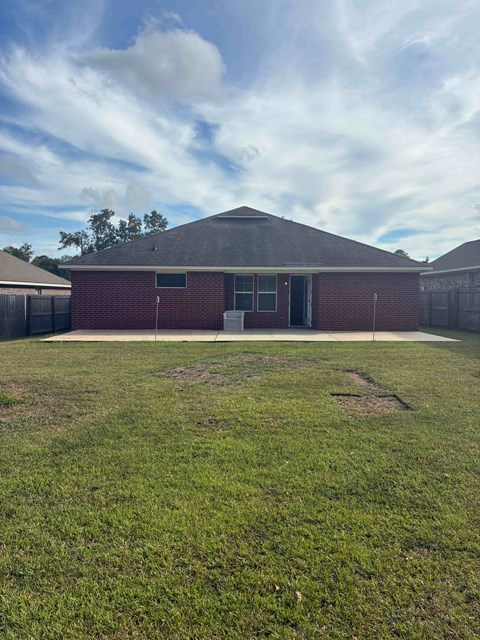 A red brick building with a grey roof and a green lawn in front.