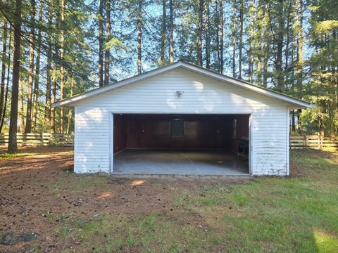 A white garage with a brown door is situated in a grassy area with trees in the background.
