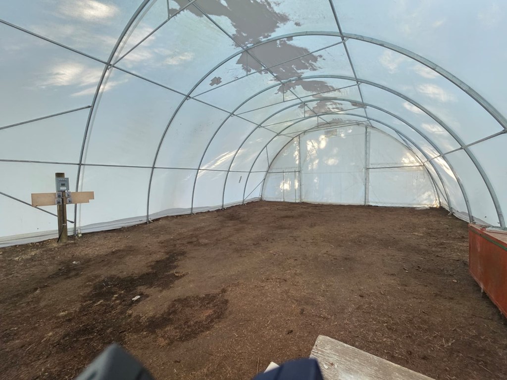 A greenhouse with soil inside and a wooden post.