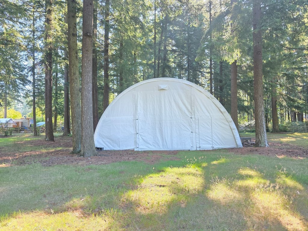 A white dome tent is set up in a grassy area surrounded by trees.