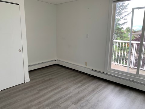 A room with a white door and a window with a view of a balcony.