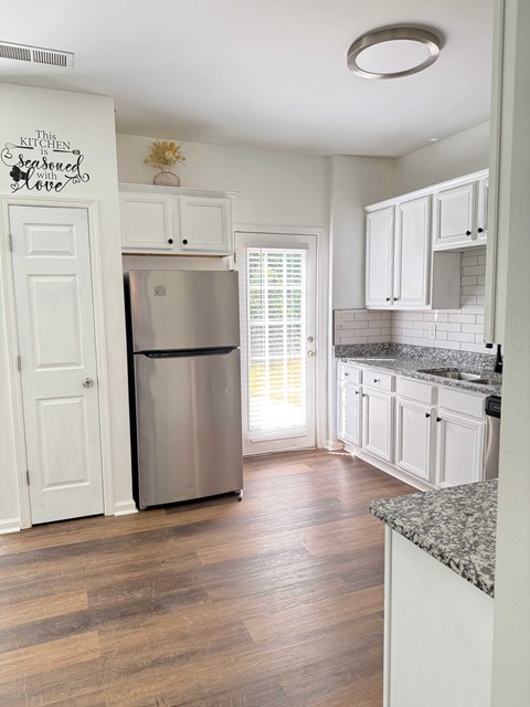 A kitchen with white cabinets and a wooden floor.