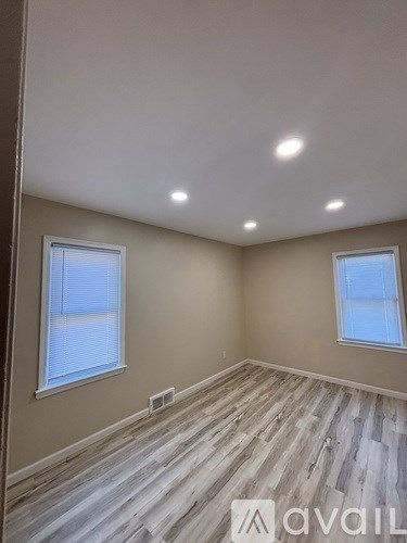 A room with wooden flooring and two windows.