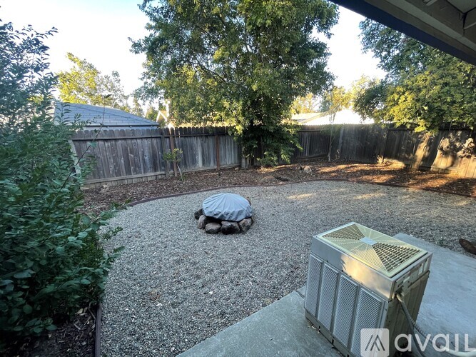 A backyard with a gravel area, a tree, and a fence.