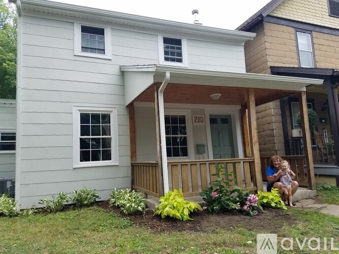 A woman and a child are sitting on the porch of a house with the number 210 on it.