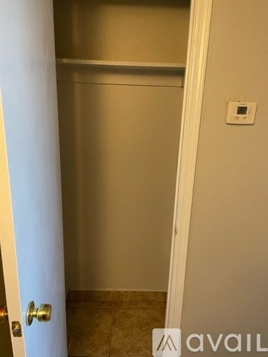 A white door with a gold handle is open to a small, empty room with a tiled floor.