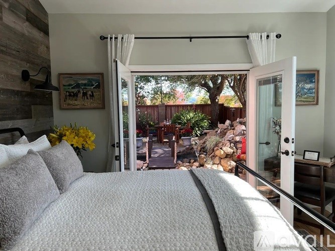 A bedroom with a large bed and a view of a backyard through a sliding glass door.